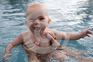 Beautiful, sweet baby boy swimming in the swimming pool holding fathers hands.