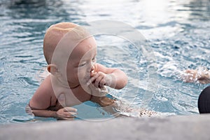 Beautiful, sweet baby boy swimming in the swimming pool holding fathers hands.