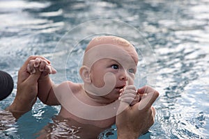 Beautiful, sweet baby boy swimming in the swimming pool holding fathers hands.