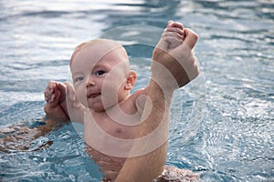 Beautiful, sweet baby boy swimming in the swimming pool holding fathers hands.