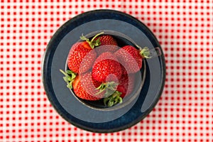 Beautiful, sweet, freshly picked strawberries in a ceramic cup and saucer on a checkered tablecloth. Organic garden berries