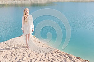 Beautiful sweet gentle girl in white dress in light big pink hat on the shore of the blue sea at sunset summer evening sun