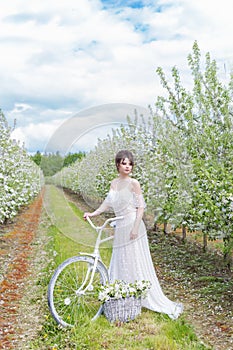 Beautiful sweet gentle happy girl in a beige dress with a boudoir with a white bicycle with flowers in the basket , modern photo