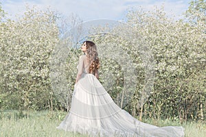 Beautiful sweet girl bride in a tender air wedding dress in a blooming spring garden in the rays of sunlight at sunset. Fine art