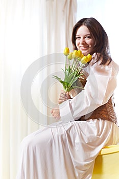 Beautiful sweet girl in nightgown in early morning with bouquet of delicate yellow tulips. Gift on International