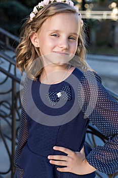 Beautiful sweet girl schoolgirl in school uniform outside on a sunny day with curly hair and a wreath of delicate roses in her hai