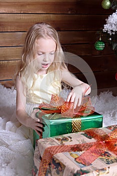 Beautiful sweet girl sits near a Christmas tree. She opens the gift.