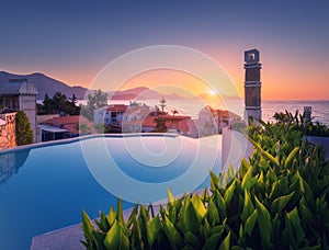 Beautiful swimming pool, green bush and orange roofs at sunset