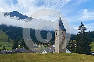 Beautiful swiss alpine countryside with a medieval bell tower with a clock and Rothorn mountain on background in