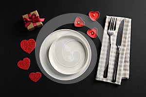 Beautiful table setting with burning candles and decorative hearts on black table for romantic dinner, flat lay