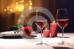 Beautiful table setting with glasses of wine, candles and rose against blurred lights. Romantic dinner for Valentine`s day