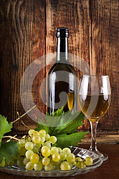 Table white wine in glass and black bottle on desk with grape