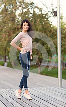 Beautiful tall girl with long hair brunette in jeans standing on old wooden planks on a warm summer evening