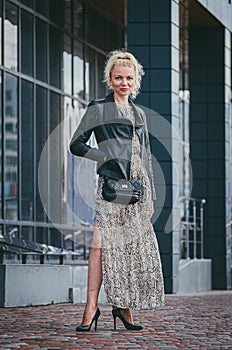 Beautiful tall slim woman blonde in a trendy long dress with a reptile print snake, in a leather jacket with high heels, walks