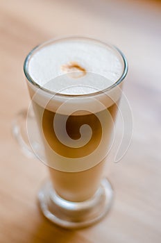 Beautiful tall transparent glass containing latte coffee drink on table in cafe in front of window with natural light