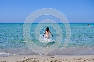 Beautiful tanned girl in a bikini at the beach running into the crystal clear water