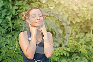 Beautiful tanned happy teen girl listening to music in headphones in nature in the summer.