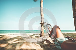 Beautiful Tanned legs of women. relax on hammock at sandy tropical beach.