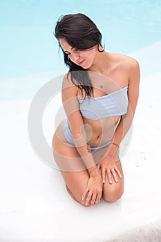 beautiful tanned sporty slim woman relaxing in white swimming pool with amazing blue water during vacation time