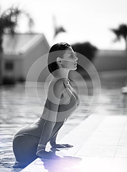 Beautiful tanned woman in blue swimwear relaxing in swimming pool spa near expensive villa on hot summer day