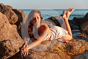 A beautiful tanned woman in her underwear lies on the coastal rocks. The sea in the background. Sunset