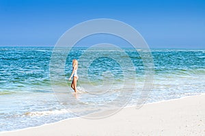 Beautiful tanned woman in swimsuit is walking on the ocean beach