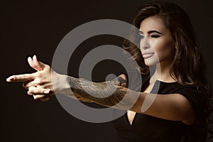 Beautiful tattooed woman with luxuriant shining wavy hair and perfect make up pretending to aim something with shooting gesture photo