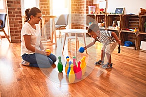 Beautiful teacher and toddler boy playing bowling at kindergarten