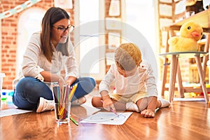 Beautiful teacher and toddler drawing using pencils and paper around lots of toys at kindergarten