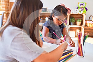 Beautiful teacher and toddler girl drawing draw using colored pencils at kindergarten