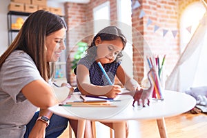 Beautiful teacher and toddler girl drawing draw using colored pencils at kindergarten