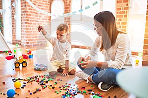 Beautiful teacher and toddler playing with building blocks around lots of toys at kindergarten