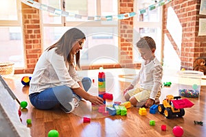 Beautiful teacher and toddler playing with building blocks around lots of toys at kindergarten
