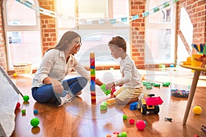 Beautiful teacher and toddler playing with building blocks around lots of toys at kindergarten