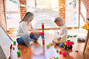 Beautiful teacher and toddler playing with building blocks around lots of toys at kindergarten