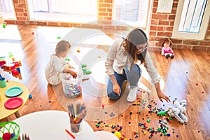 Beautiful teacher and toddler playing with building blocks around lots of toys at kindergarten