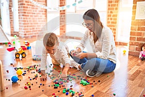 Beautiful teacher and toddler playing with building blocks around lots of toys at kindergarten