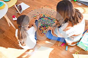 Beautiful teacher and toddler playing with building blocks toy around lots of toys at kindergarten