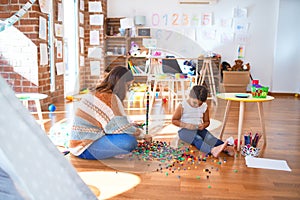 Beautiful teacher and toddler playing with building blocks toy around lots of toys at kindergarten