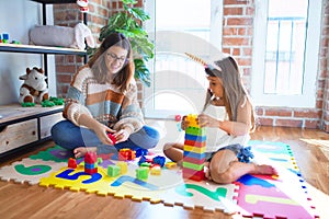 Beautiful teacher and toddler playing with building blocks toy around lots of toys at kindergarten