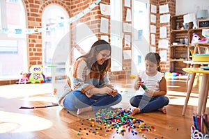 Beautiful teacher and toddler playing with building blocks toy around lots of toys at kindergarten