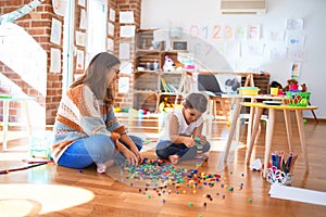 Beautiful teacher and toddler playing with building blocks toy around lots of toys at kindergarten