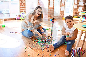 Beautiful teacher and toddler playing with building blocks toy around lots of toys at kindergarten