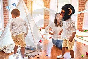 Beautiful teacher and toddlers playing with monkey mask around lots of toys at kindergarten