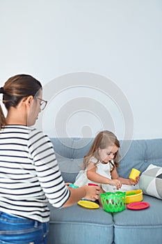 Beautiful teacher woman and toddler sitting on the sofa playing with food toys at home