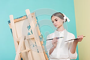 beautiful teen artist painting on easel with brush and palette