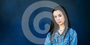 A beautiful teen brunette girl with a serious look and head tilt against a dark blue background with copy space as a