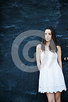 A beautiful teen brunette girl with a serious look leaning against a wall in thought