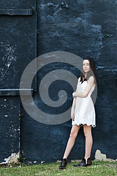 A beautiful teen brunette girl with a serious look leaning against a wall in thought