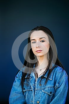 A beautiful teen brunette girl with a serious look leaning against a wall in thought with a dark navy blue background